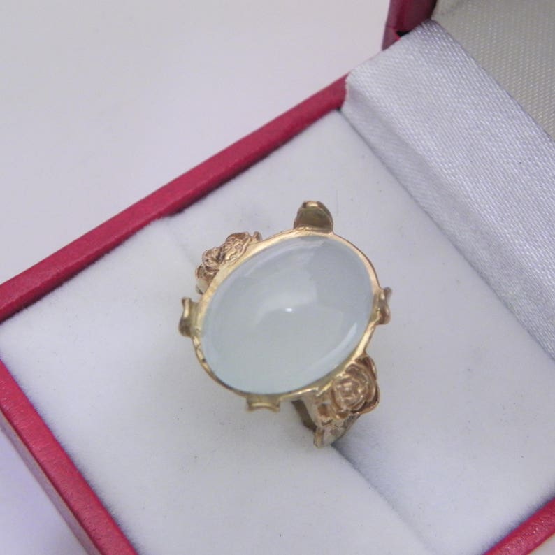Puede incluir: Un anillo de oro con una gran piedra preciosa ovalada blanca engastada en un dise&ntilde;o floral.
