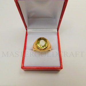 Puede incluir: Un anillo de oro con una gran piedra preciosa verde de forma ovalada engastada en una banda de oro texturizada. El anillo se presenta en una caja de anillo de terciopelo rojo.