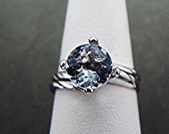 May include: A silver ring with a light blue gemstone set in a prong setting. The band is twisted and has a polished finish.