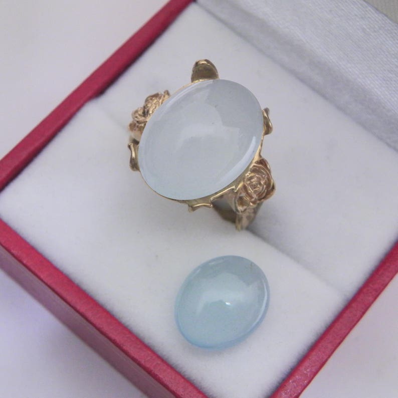 Puede incluir: Un anillo de oro con una gran piedra ovalada de aguamarina engastada en un dise&ntilde;o floral. Tambi&eacute;n se muestra una piedra de aguamarina m&aacute;s peque&ntilde;a.