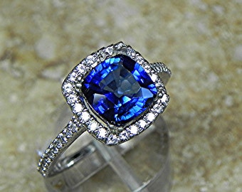 May include: A silver ring featuring a large, cushion-cut blue sapphire encircled by a halo of smaller diamonds.