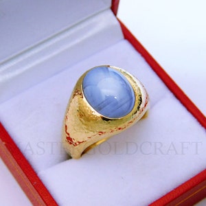 Puede incluir: Un anillo de oro con una gran piedra preciosa azul de forma ovalada engastada en el centro. El anillo est&aacute; en una caja de terciopelo rojo.