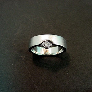 May include: A silver wedding band with a single diamond set in the center.
