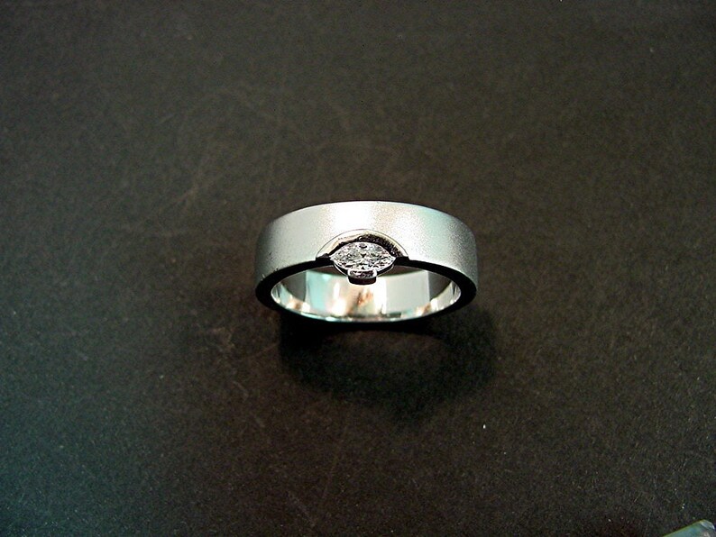 May include: A silver wedding band with a single diamond set in the center.