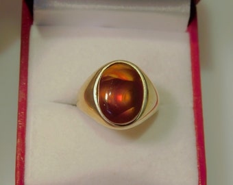 May include: A gold ring with a large oval-shaped red and orange gemstone set in a bezel setting.
