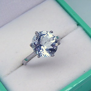 May include: A silver ring with a large, round, light blue aquamarine gemstone set in a six-prong setting.
