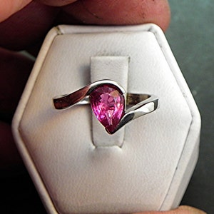 May include: A silver ring with a pink pear-shaped gemstone set in a curved band.