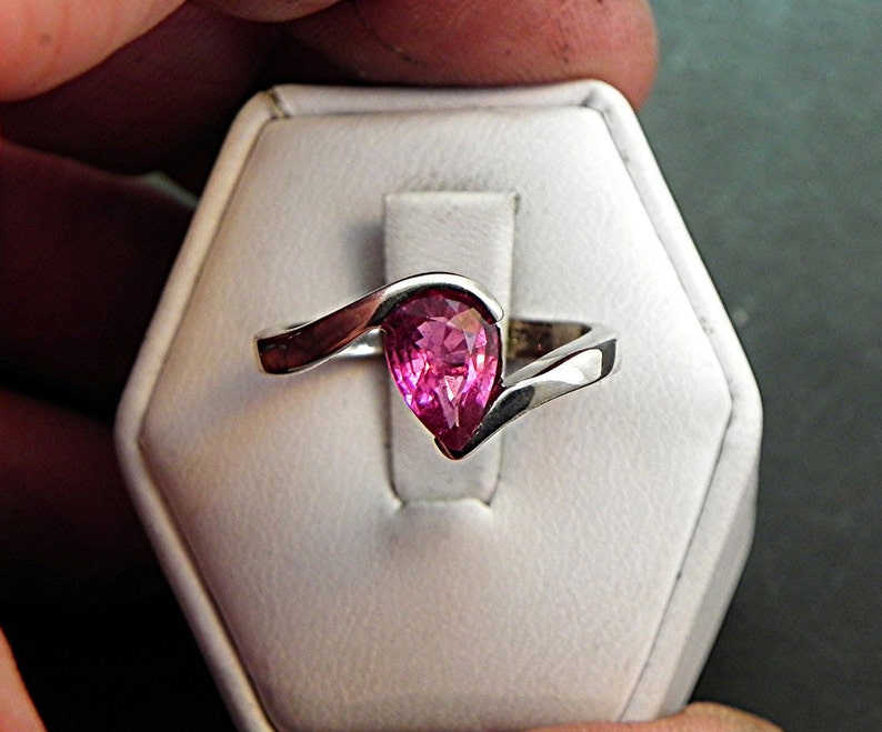 May include: A silver ring with a pink pear-shaped gemstone set in a curved band.