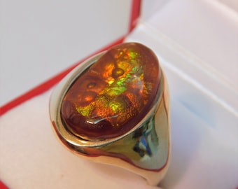 May include: A gold ring with a large oval-shaped gemstone. The gemstone is a mix of red, orange, green, and gold colors. The ring is in a red and white box.