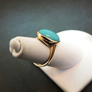May include: A gold ring with a turquoise oval gemstone set in a bezel setting.