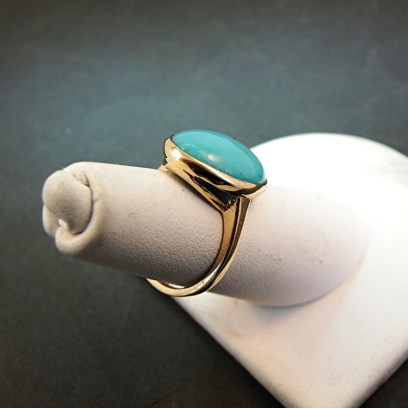 May include: A gold ring with a turquoise oval gemstone set in a bezel setting.
