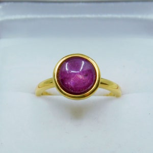 May include: A gold ring featuring a large, oval ruby gemstone set in a bezel setting.