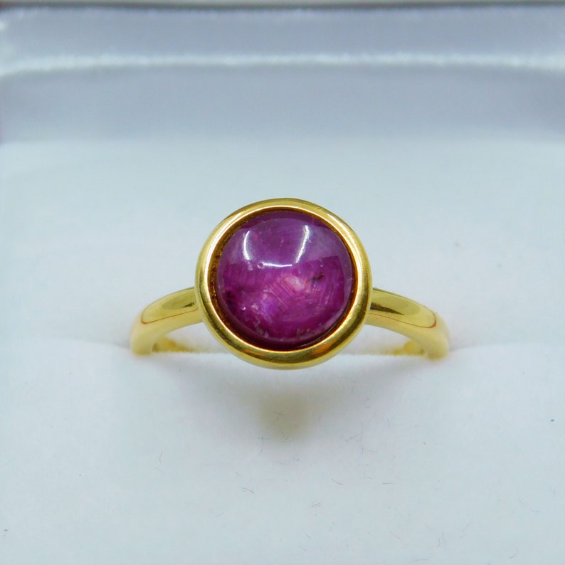 May include: A gold ring featuring a large, oval ruby gemstone set in a bezel setting.