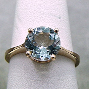 May include: A gold ring with a large, round, light blue aquamarine gemstone.