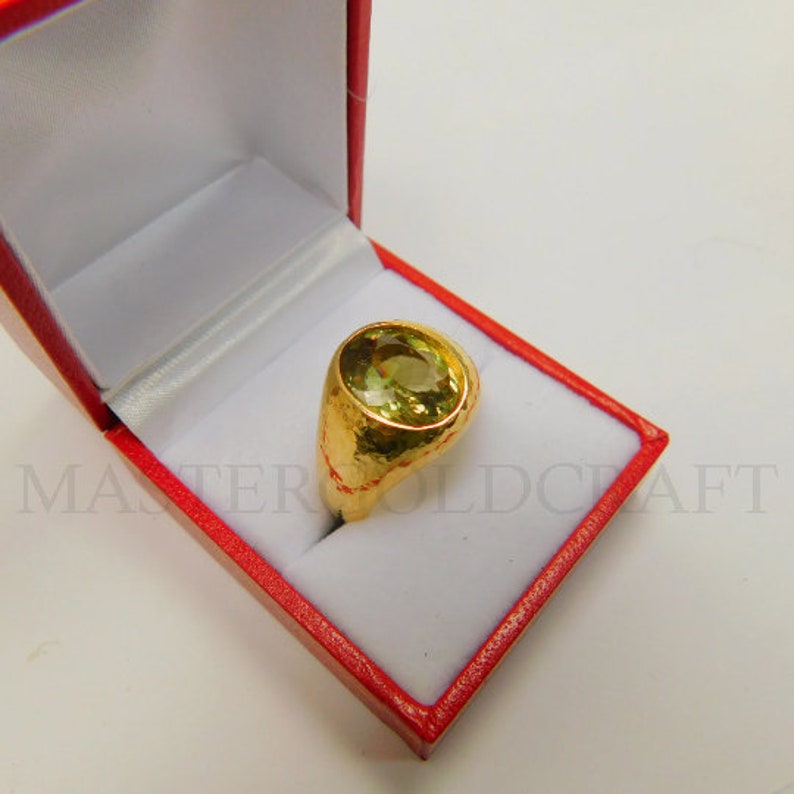 Puede incluir: Un anillo de oro con una gran piedra preciosa verde de forma ovalada. El anillo est&aacute; en una caja de anillo de terciopelo rojo.