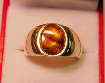 May include: A gold ring with a large oval-shaped gemstone. The gemstone is a fiery orange color with a swirling pattern.