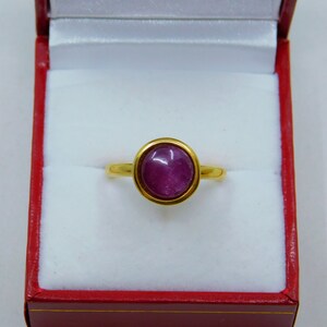 May include: A gold ring with a purple gemstone set in a bezel setting.