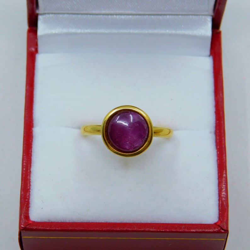 May include: A gold ring with a purple gemstone set in a bezel setting.