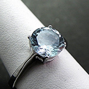 May include: A silver ring with a large, round, light blue aquamarine gemstone.