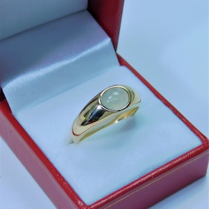 K&ouml;nnte beinhalten: Ein goldener Ring mit einem wei&szlig;en Edelstein, der in einer Zargenfassung gefasst ist. Der Ring befindet sich in einer roten Samt-Ringbox.