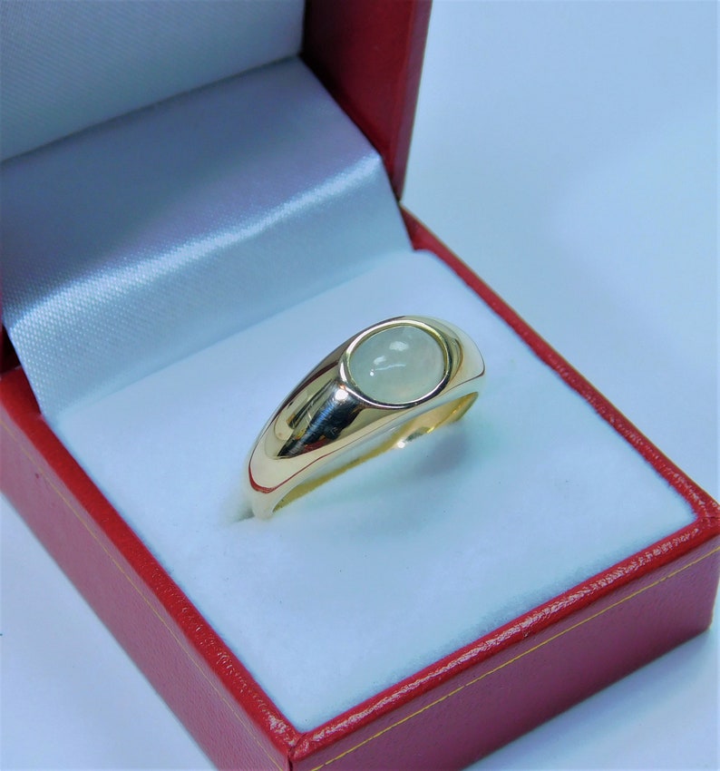 K&ouml;nnte beinhalten: Ein goldener Ring mit einem wei&szlig;en Edelstein, der in einer Zargenfassung gefasst ist. Der Ring befindet sich in einer roten Samt-Ringbox.