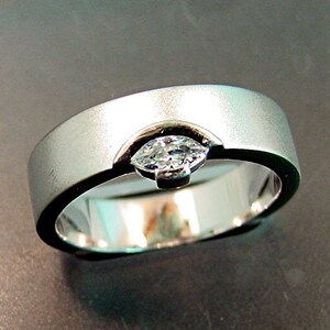 May include: A silver wedding band with a single, clear, marquise-shaped diamond set in the center.