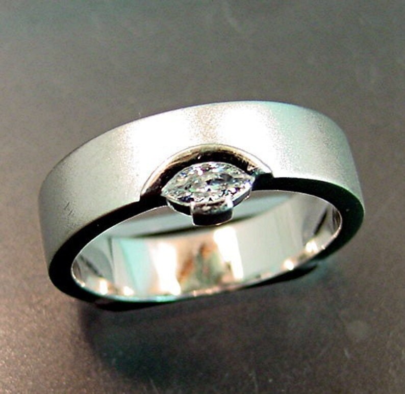 May include: A silver wedding band with a single, clear, marquise-shaped diamond set in the center.