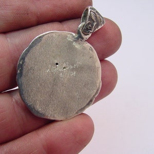May include: Silver pendant with a round, textured surface. The back of the pendant has the inscription "A. Albert 1911-1933".