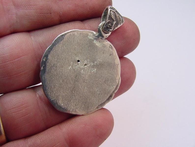 May include: Silver pendant with a round, textured surface. The back of the pendant has the inscription "A. Albert 1911-1933".