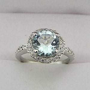 Puede incluir: Un anillo de plata con una gran piedra de aguamarina redonda rodeada por un halo de diamantes más pequeños.