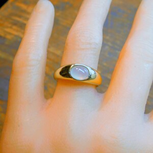 K&ouml;nnte beinhalten: Ein goldener Ring mit einem hellrosa ovalen Edelstein, der in einer Zargenfassung gefasst ist.