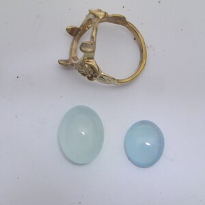 Puede incluir: Dos piedras preciosas ovaladas de color azul claro, una m&aacute;s grande que la otra, y un engaste de anillo de oro.