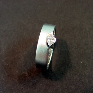 May include: A silver ring with a single, clear, oval-shaped gemstone set in the center.