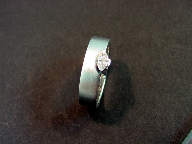 May include: A silver ring with a single, clear, oval-shaped gemstone set in the center.