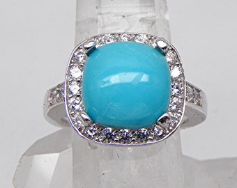 May include: A silver ring with a large turquoise gemstone surrounded by a halo of smaller clear gemstones.