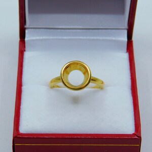 May include: A gold ring setting with a round bezel, ready to be set with a gemstone. The ring is displayed in a red velvet box.