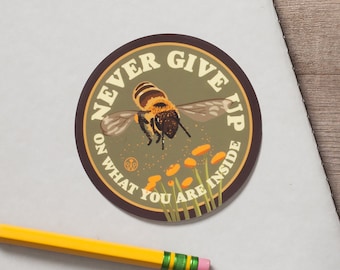 May include: A round sticker with a green background and a brown border. The sticker features a bee flying with the text "Never Give Up On What You Are Inside".
