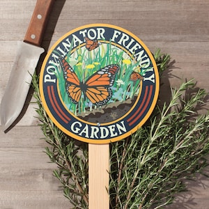 A round yard sign mounted to a wood stake featuring a monarch butterfly and native plants, and text that reads: Pollinator Friendly Garden.