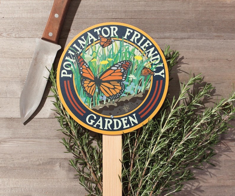A round yard sign mounted to a wood stake featuring a monarch butterfly and native plants, and text that reads: Pollinator Friendly Garden.