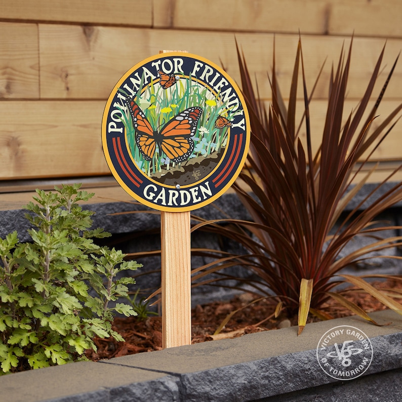 A round yard sign mounted to a wood stake featuring a monarch butterfly and native plants, and text that reads: Pollinator Friendly Garden.