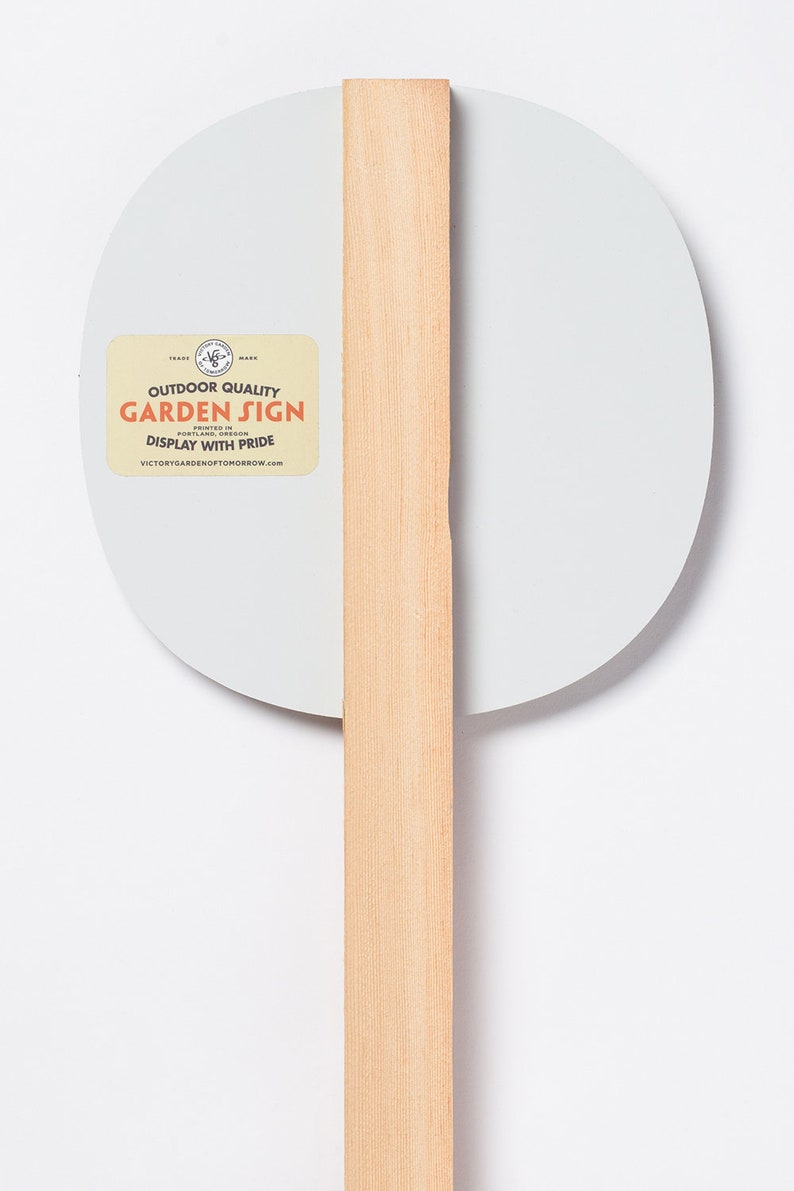 May include: A white round garden sign with a wooden stake. The sign has a sticker that says "Outdoor Quality Garden Sign Printed in Portland, Oregon Display with Pride VictoryGardenofTomorrow.com".
