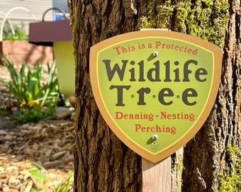 May include: A brown tree trunk with a green moss covered area. A yellow and green sign is attached to the tree with the text "This is a Protected Wildlife Tree. Denning. Nesting. Perching."