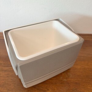 May include: A rectangular ice bucket with a white interior and a grey exterior. The bucket has a textured surface and a white rim. The design is simple and functional, suitable for keeping beverages cold.