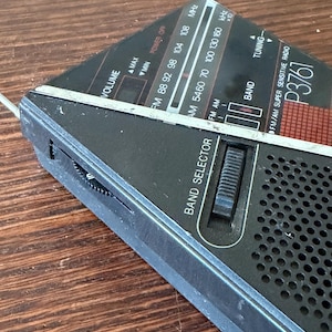 May include: A black and silver vintage radio with a triangular design. The radio features a volume control, band selector, and tuning dial. The radio has the text "FM/AM SUPER SENSITIVE RADIO P3761" and frequency indicators.