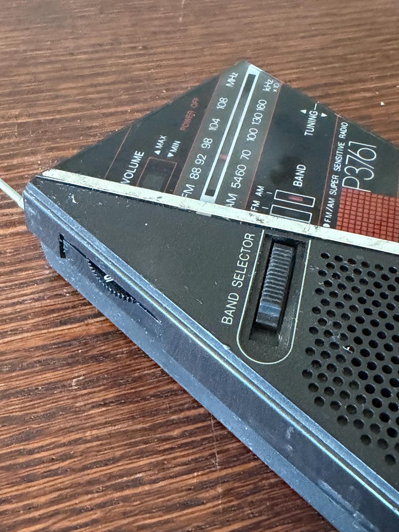 May include: A black and silver vintage radio with a triangular design. The radio features a volume control, band selector, and tuning dial. The radio has the text "FM/AM SUPER SENSITIVE RADIO P3761" and frequency indicators.