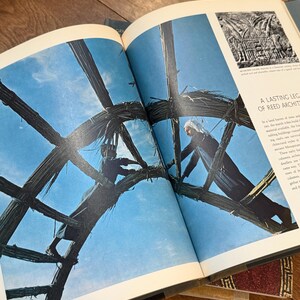 May include: Open book with a photograph of two people working on a reed structure against a blue sky. The text "A LASTING LEG OF REED ARCHIT" is visible on the page. The book is open on a wooden surface.