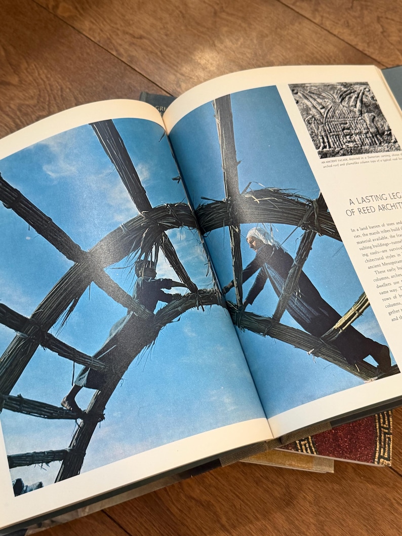 May include: Open book with a photograph of two people working on a reed structure against a blue sky. The text "A LASTING LEG OF REED ARCHIT" is visible on the page. The book is open on a wooden surface.