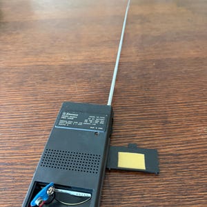 May include: A black Emerson radio with an extended silver antenna. The battery compartment is open, revealing a 9-volt battery. The radio's model number is F370, and it has a power source range.