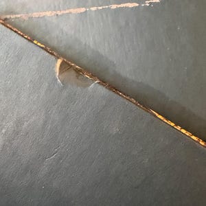 May include: Close-up of a dark teal surface with a diagonal, thin, brown line with yellow accents. A lighter, faded line is above it. A small piece of the surface is torn away.