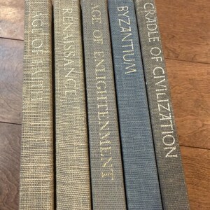 May include: A collection of five hardcover books with titles in gold lettering: "Age of Faith," "Renaissance," "Age of Enlightenment," "Byzantium," and "Cradle of Civilization." The books have textured covers in shades of beige and blue.